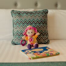 Plush toy and children's book on a neatly made bed with a zigzag patterned cushion.