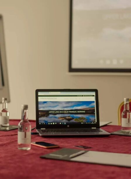 Conference room at Scotts Hotel Killarney with laptop, water bottles, and notepads on a red table.