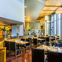 Bright hotel dining area with wooden tables, leather chairs, and decorative plants.