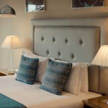 Elegant hotel room with plush bed, blue cushions, and warm ambient lighting.