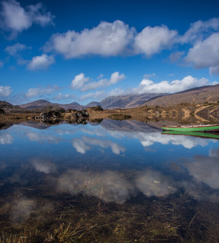 Tranquil Killarney lake view with blue sky and green boat, perfect for relaxation.