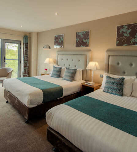 Spacious hotel room with two double beds, elegant decor, and a scenic balcony view.