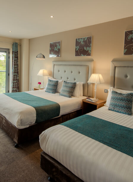 Spacious hotel room with two double beds, elegant decor, and a scenic balcony view.