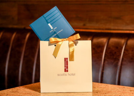 Gift bag with a gold ribbon from Scotts Hotel Killarney, placed on a cosy booth seat.