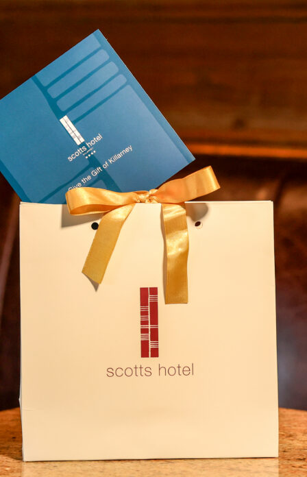 Gift bag with a gold ribbon from Scotts Hotel Killarney, placed on a cosy booth seat.