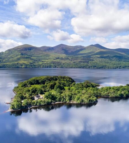 Aerial view of a lush island on a calm lake with mountains in the background at Killarney.
