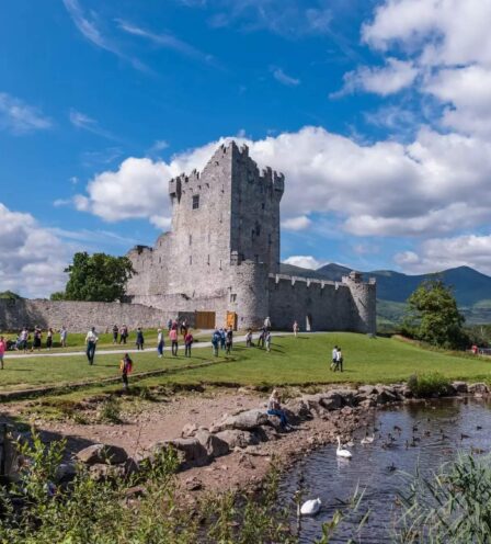 Visitors enjoy a sunny day by the historic castle near a serene lake at Scotts Hotel Killarney.