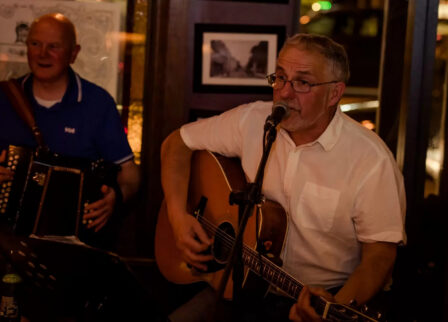 Two musicians playing guitar and accordion in a cosy, dimly lit setting at Scotts Hotel Killarney.