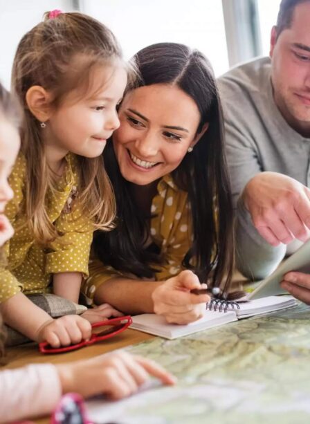 Family planning activities using a tablet and map in a cosy hotel room.