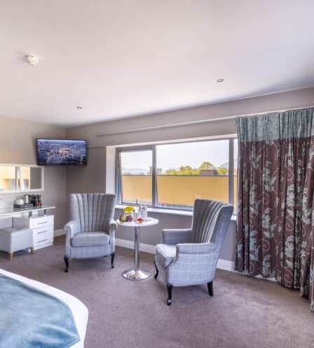 Spacious hotel room with plush chairs, large windows, and a scenic view, offering a cosy retreat.