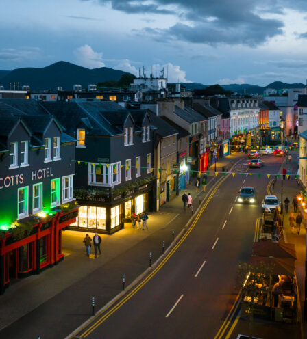 Evening view of Scotts Hotel Killarney, with people strolling and cars on a lively street.