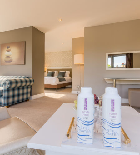 Spacious hotel room with cosy seating, modern decor, and complimentary water bottles.
