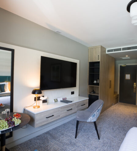 Elegant hotel room with plush bedding, a modern desk, fruit display, and ambient lighting.