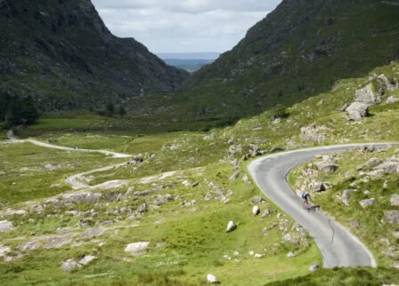 Cyclist on winding road in scenic Killarney valley surrounded by lush green hills.