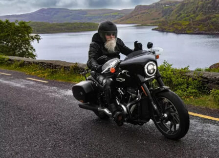 Rider cruises scenic road near lake and hills.