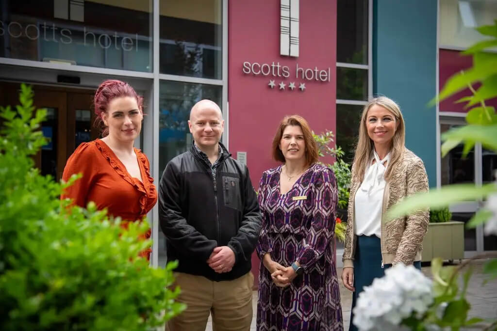 Hotel staff smiling warmly outside Scotts Hotel Killarney entrance, surrounded by greenery.
