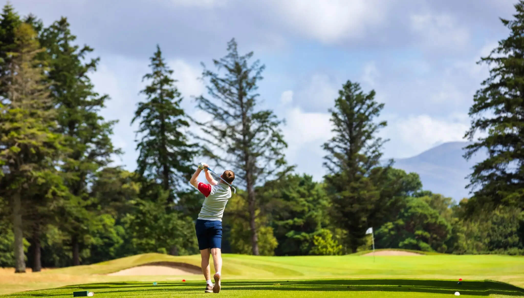 A golfer swings on a lush, scenic course with mountains in the background near Scotts Hotel Killarney.