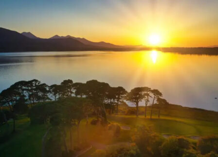 Golden sunset over tranquil lake near Scotts Hotel Killarney, surrounded by lush greenery.