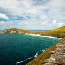 Coastal road along green cliffs with ocean views near Scotts Hotel Killarney, under blue skies.