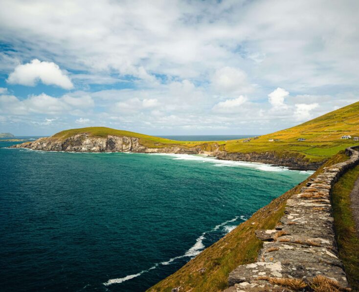 Coastal road along green cliffs with ocean views near Scotts Hotel Killarney, under blue skies.