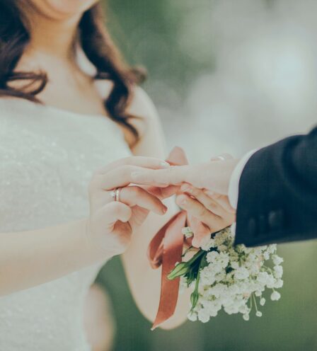 Bride placing a ring on groom’s finger in scenic outdoor setting.
