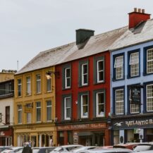 Colourful buildings in Killarney town centre with parked cars and pedestrians strolling.