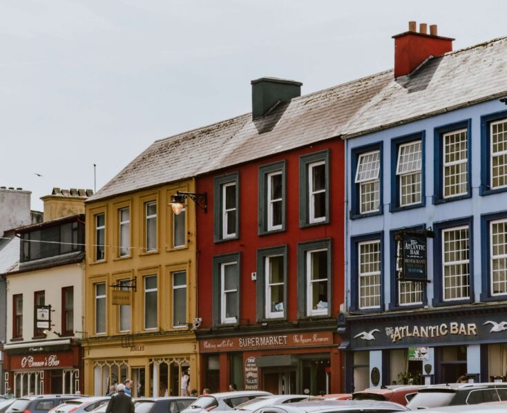 Colourful buildings in Killarney town centre with parked cars and pedestrians strolling.