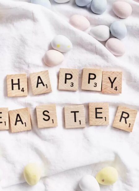 Easter message with Scrabble tiles and pastel eggs on a white fabric background.