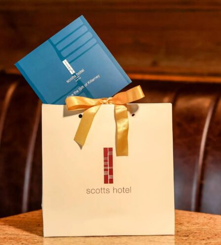 Gift bag with a blue voucher at Scotts Hotel Killarney on a cosy wooden bench.