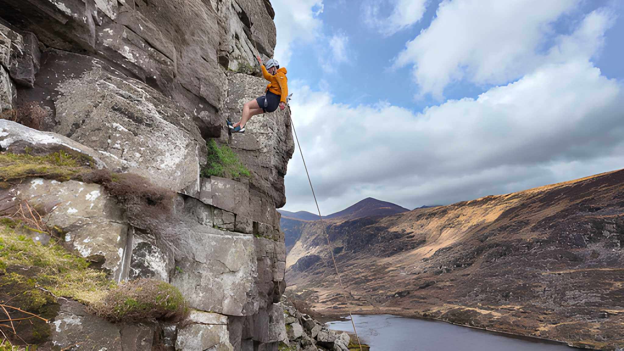 A person rock climbing in scenic Killarney mountains with a bright blue sky backdrop.