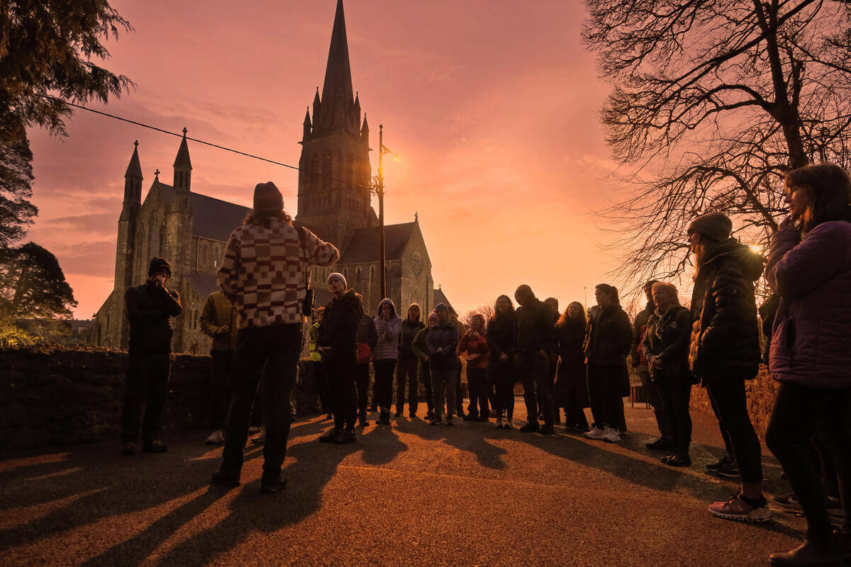 Group of people gathered at sunset near a historic church in Killarney.
