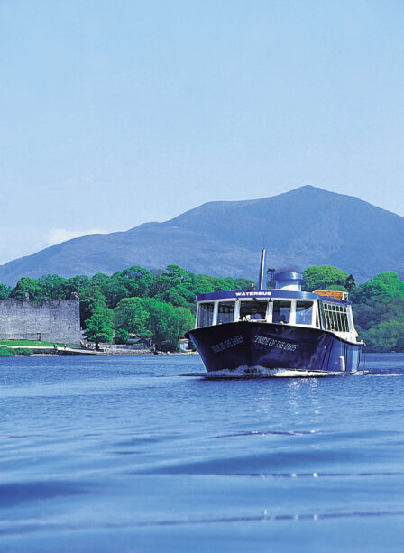 A scenic boat ride on a tranquil lake near a historic castle and lush mountains in Killarney.