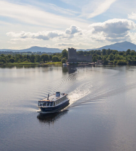 Scenic boat ride on calm lake with lush greenery and distant mountains, near Scotts Hotel Killarney.