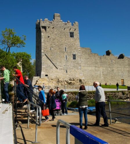 Visitors boarding a boat tour by a historic castle at Scotts Hotel Killarney.