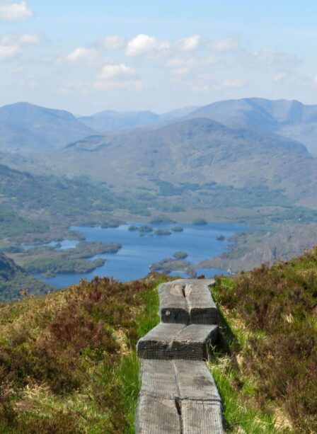 Scenic view of lush hills, lake, and wooden trail in Killarney National Park.