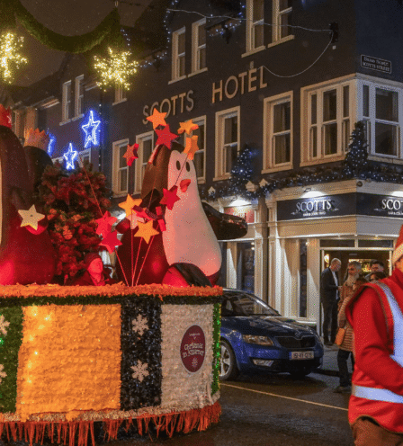 Festive parade with penguin float outside Scotts Hotel Killarney in winter evening.
