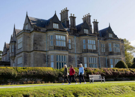 People walking in front of historic, grand Scotts Hotel Killarney on a sunny day.