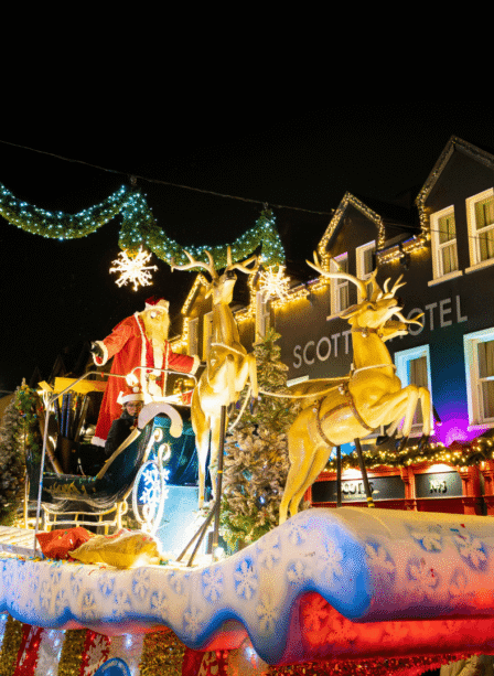 Festive crowd enjoying Christmas lights at Scotts Hotel Killarney, with a vibrant holiday parade.