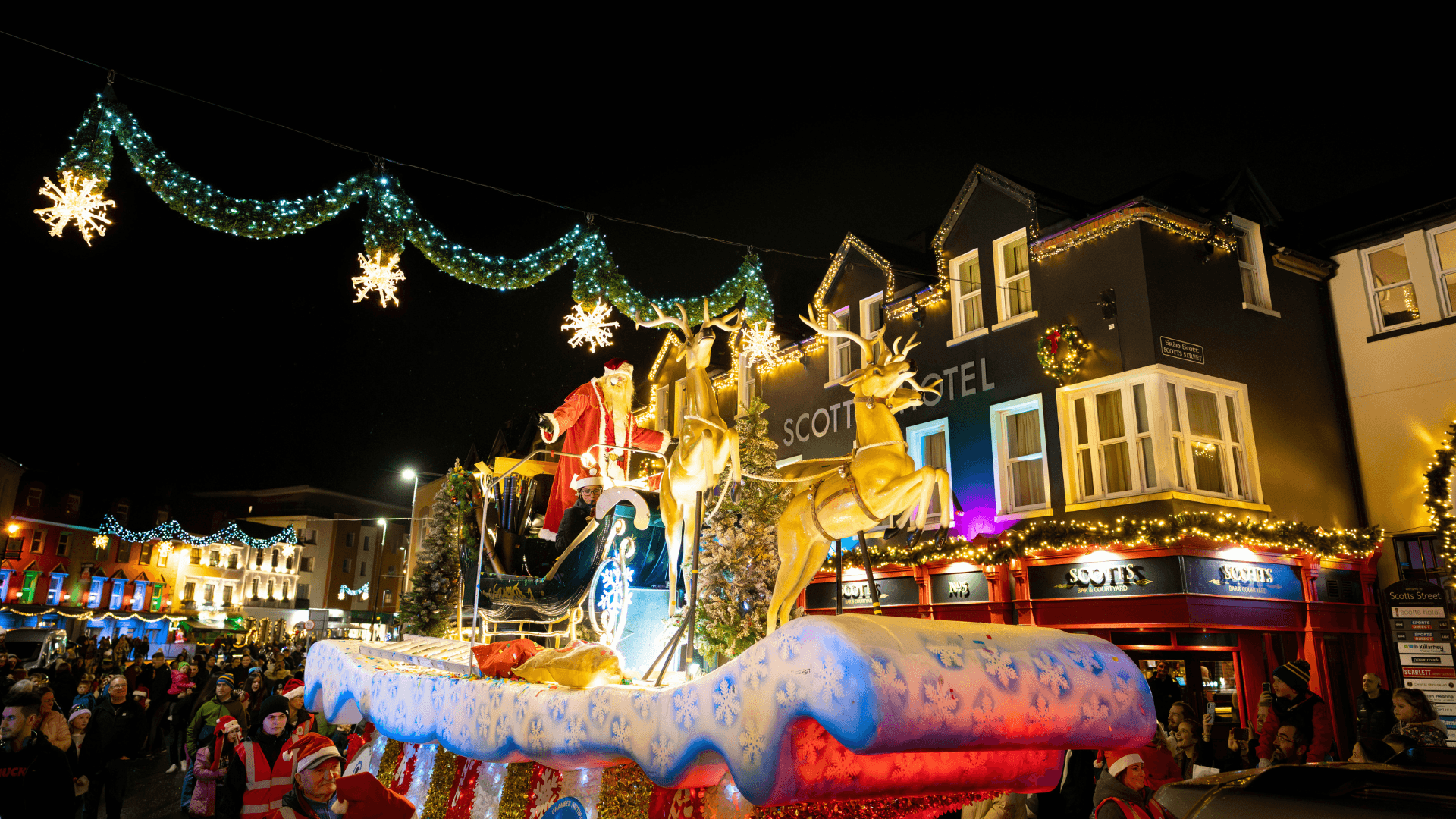 Festive crowd enjoying Christmas lights at Scotts Hotel Killarney, with a vibrant holiday parade.